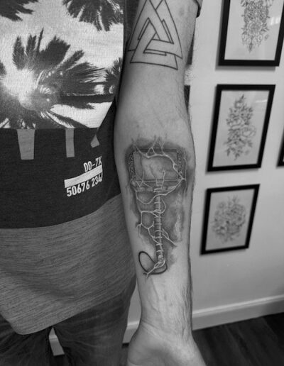 Unterarm mit anatomischem Tattoo einer Wirbelsäule und einem geometrischen Symbol oberhalb, schwarz-weiß fotografiert.