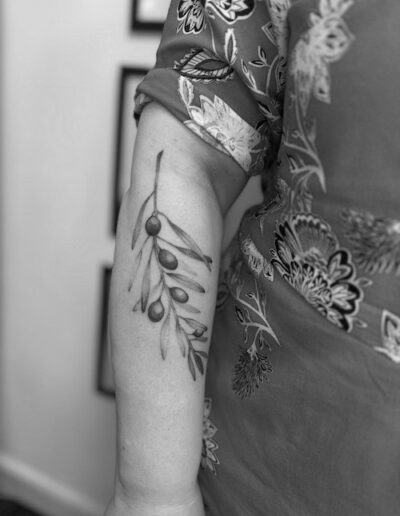 Schwarz-weiß Aufnahme eines Unterarms mit einem minimalistischen Tattoo eines Olivenzweigs.