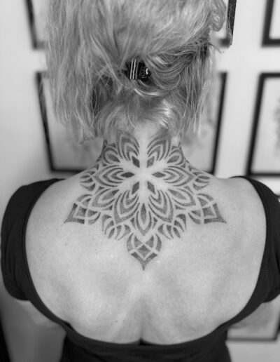 Rückenansicht einer Person mit einem geometrischen Mandala-Tattoo im Nackenbereich, schwarz-weiß fotografiert.