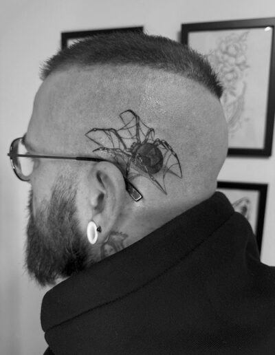 Seitliche Ansicht eines Mannes mit rasiertem Kopf und einem geometrischen Tattoo hinter dem Ohr, schwarz-weiß fotografiert.