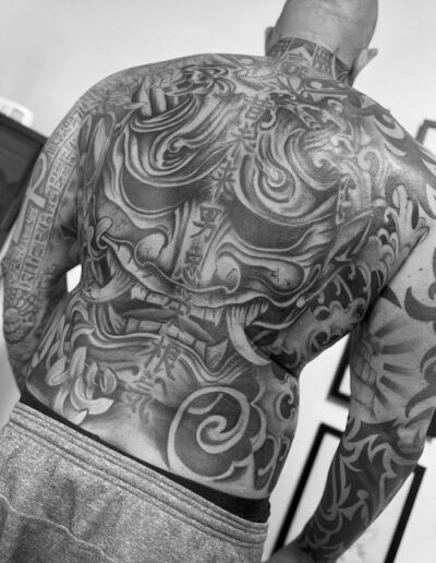 Schwarz-weiß Aufnahme eines vollständig tätowierten Rückens mit großflächigen, ornamentalen und fließenden Motiven.