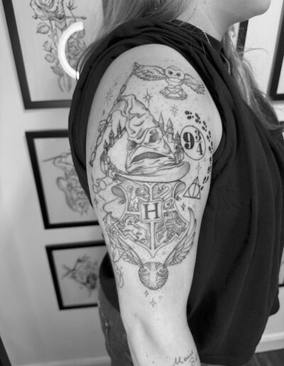 Oberarm mit einem illustrativen Tattoo aus magischen Symbolen, einer sprechenden Hutfigur und der Zahl 9¾, schwarz-weiß fotografiert.