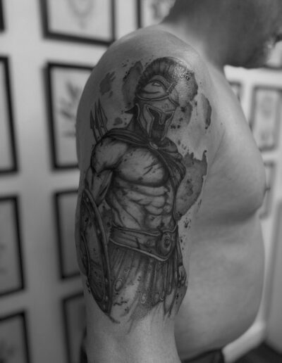 Schwarz-weiß Fotografie eines Oberarms mit einem realistischen Tattoo eines antiken Kriegers mit Helm und Schild.
